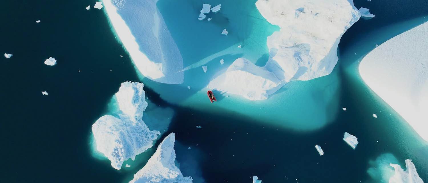 Greenland Icebergs – Mike Broermann Aerial view of icebergs with a small red boat in Greenland – photo by Mike Broermann, GroupMB Real Estate